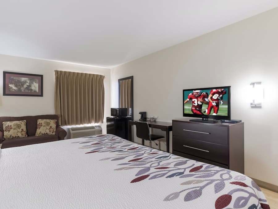 A hotel room with a bed, a desk, a television, and a window with curtains.