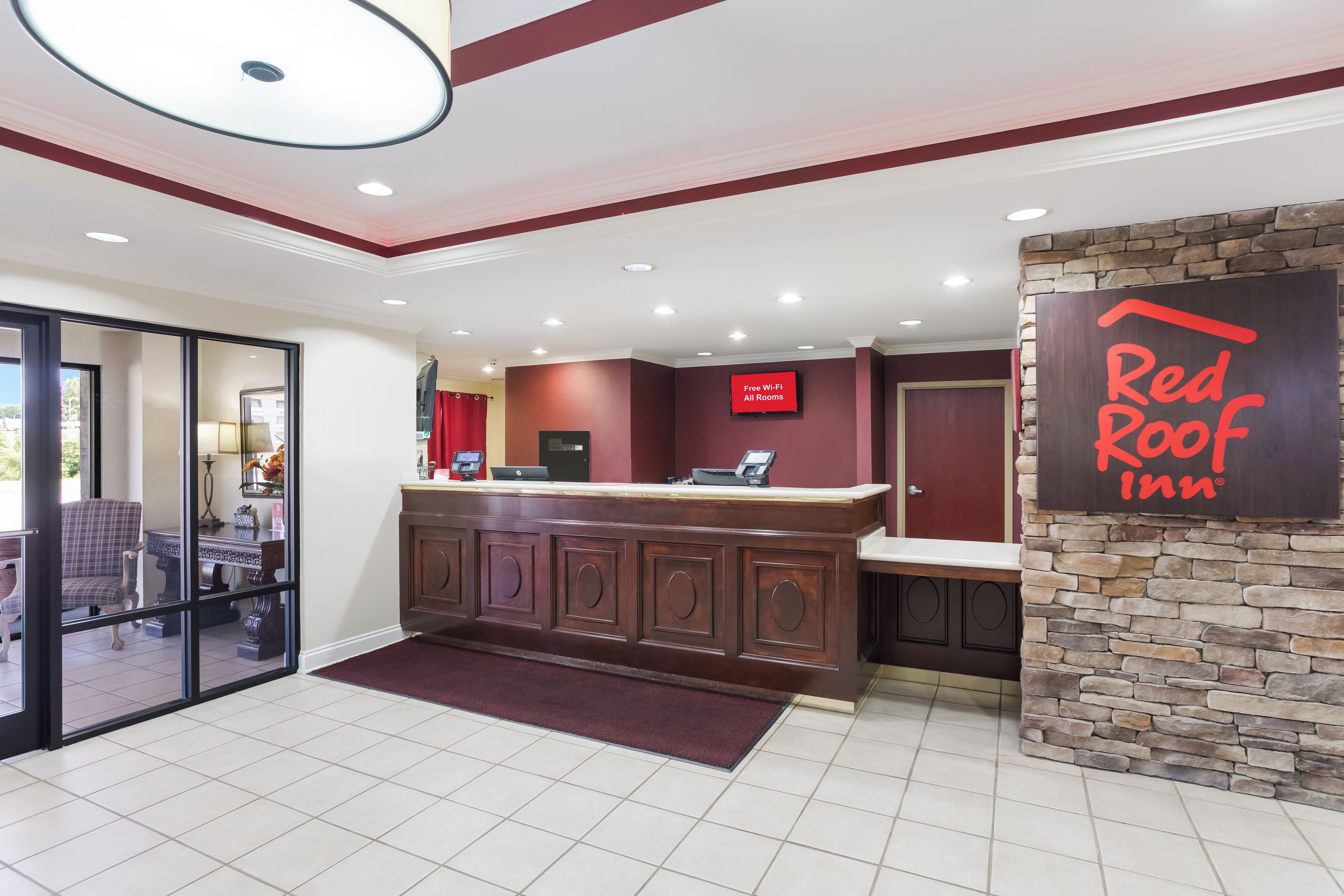 A reception area with a Red Roof Inn sign, a reception desk with a computer, a TV screen, and a stone accent wall.