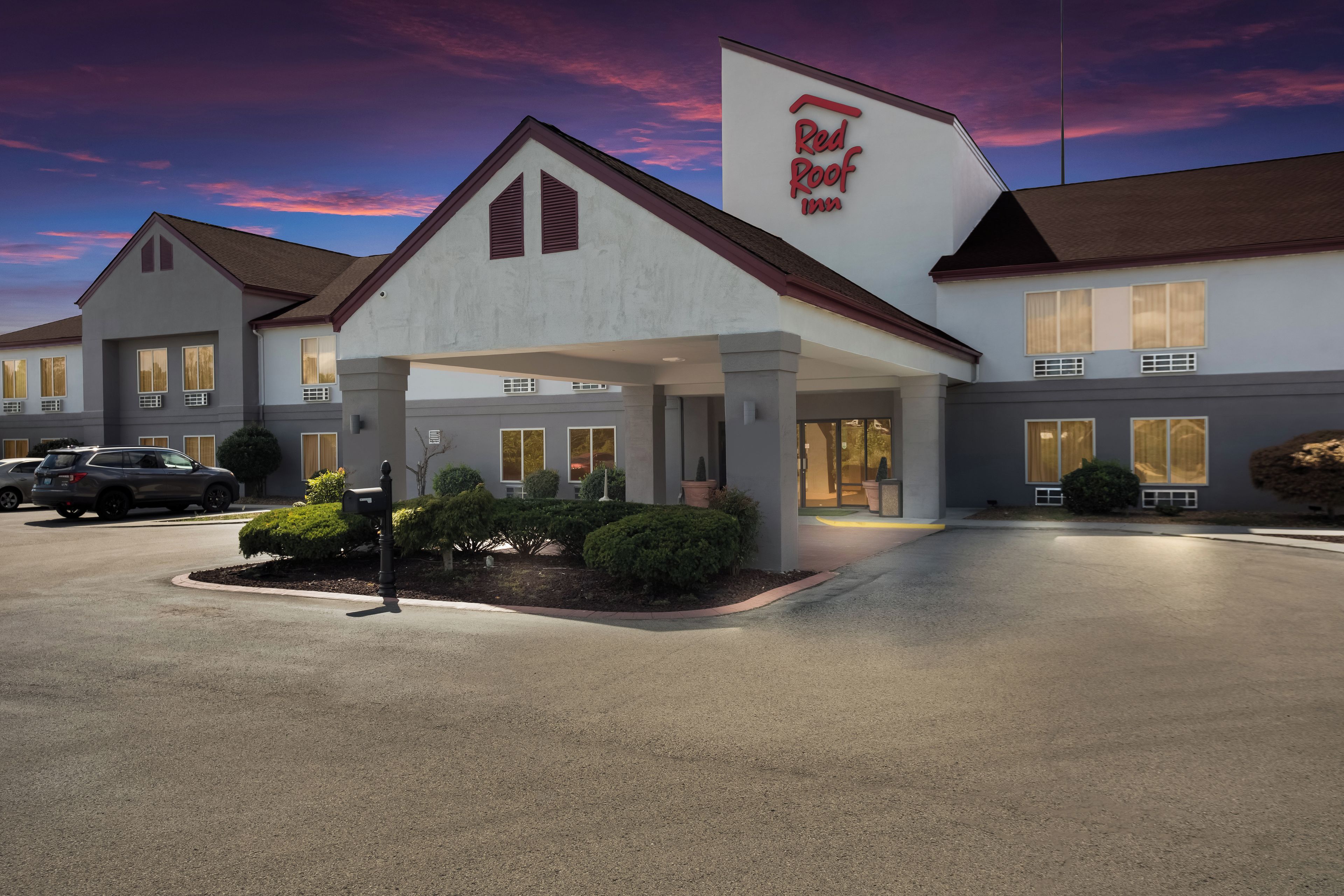 Un Red Roof Inn con entrada cubierta, varias ventanas y un área de estacionamiento.