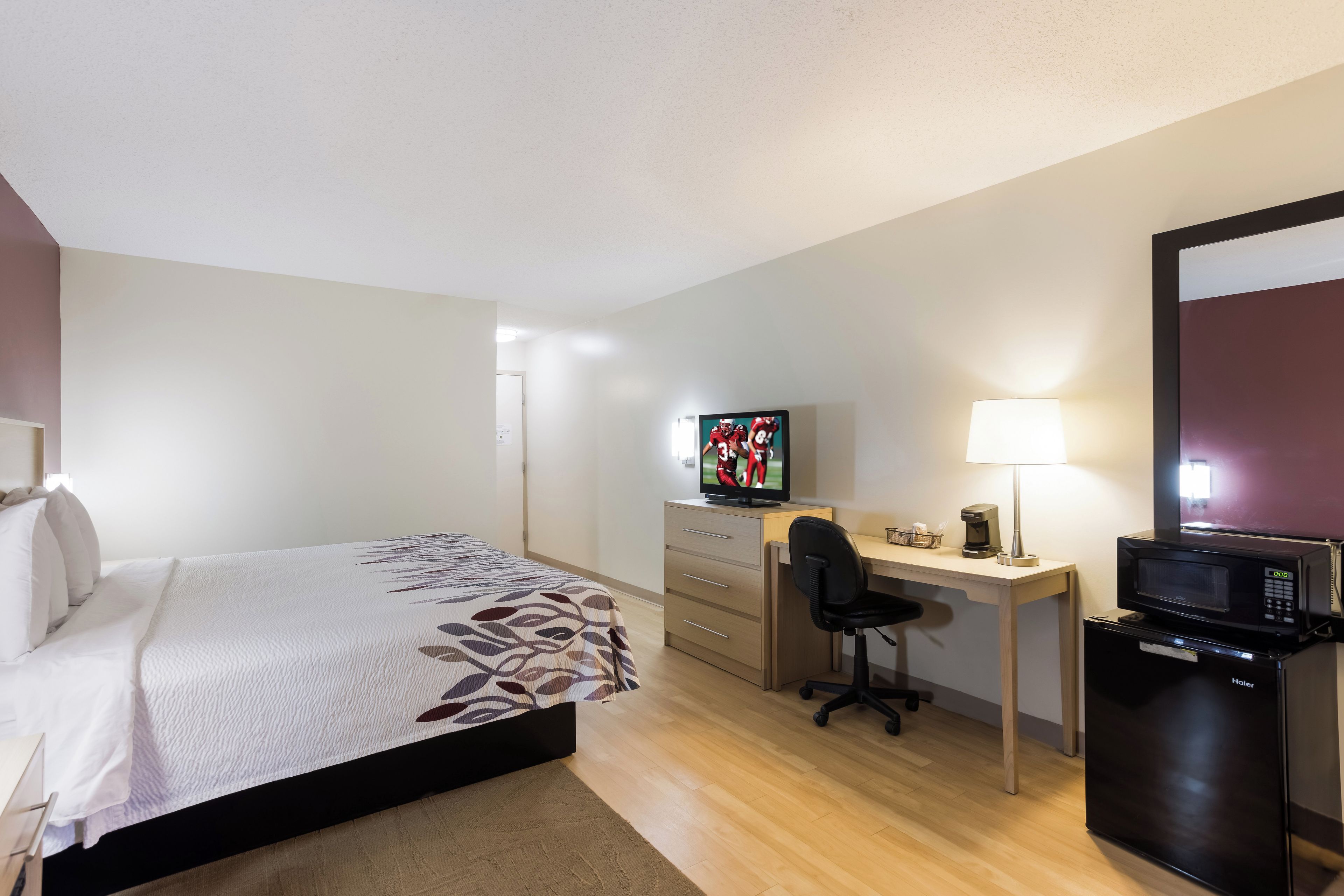 Une chambre d’hôtel équipée d’un lit, d’un bureau, d’une chaise, d’une télévision, d’une lampe et d’un réfrigérateur.