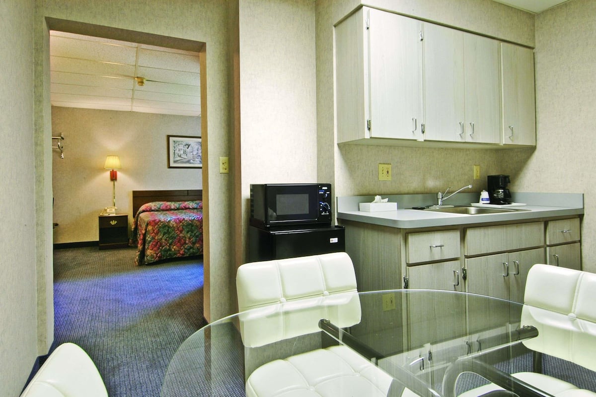 A hotel room with a bed, a desk with a computer, a microwave, a coffee maker, and a glass table with chairs.