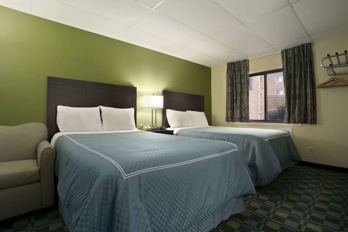 A hotel room with two beds, a sofa, a window with curtains, and a coat rack.
