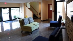 A lobby with a green sofa, a blue armchair, a staircase, and a large window.