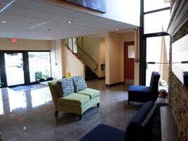 Un vestíbulo con un sofá verde, un sillón azul, una escalera y un ventanal grande.