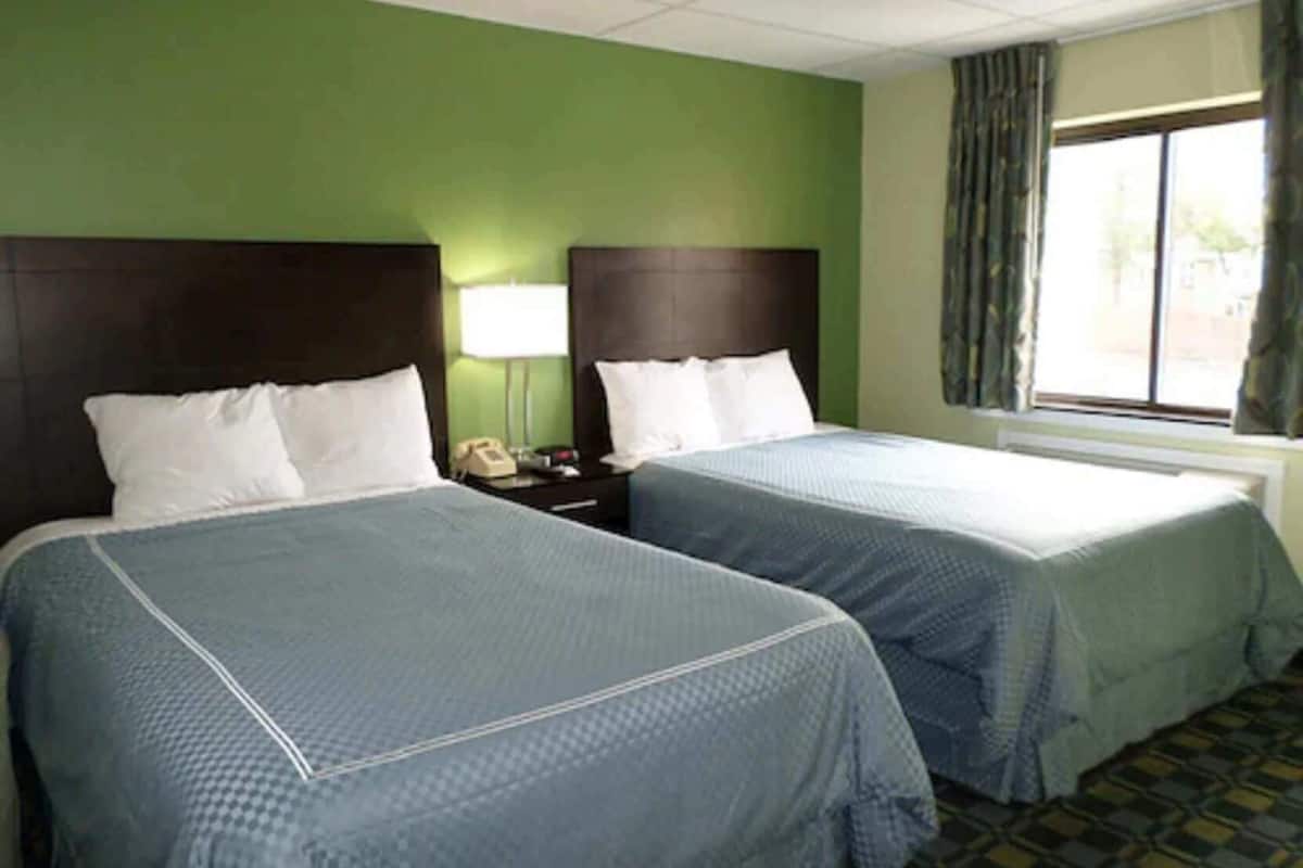 Two beds with headboards, a nightstand with a lamp, and a window with curtains.