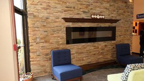 A lobby with a stone wall, a flat-screen TV, two blue armchairs, and a yellow armchair.