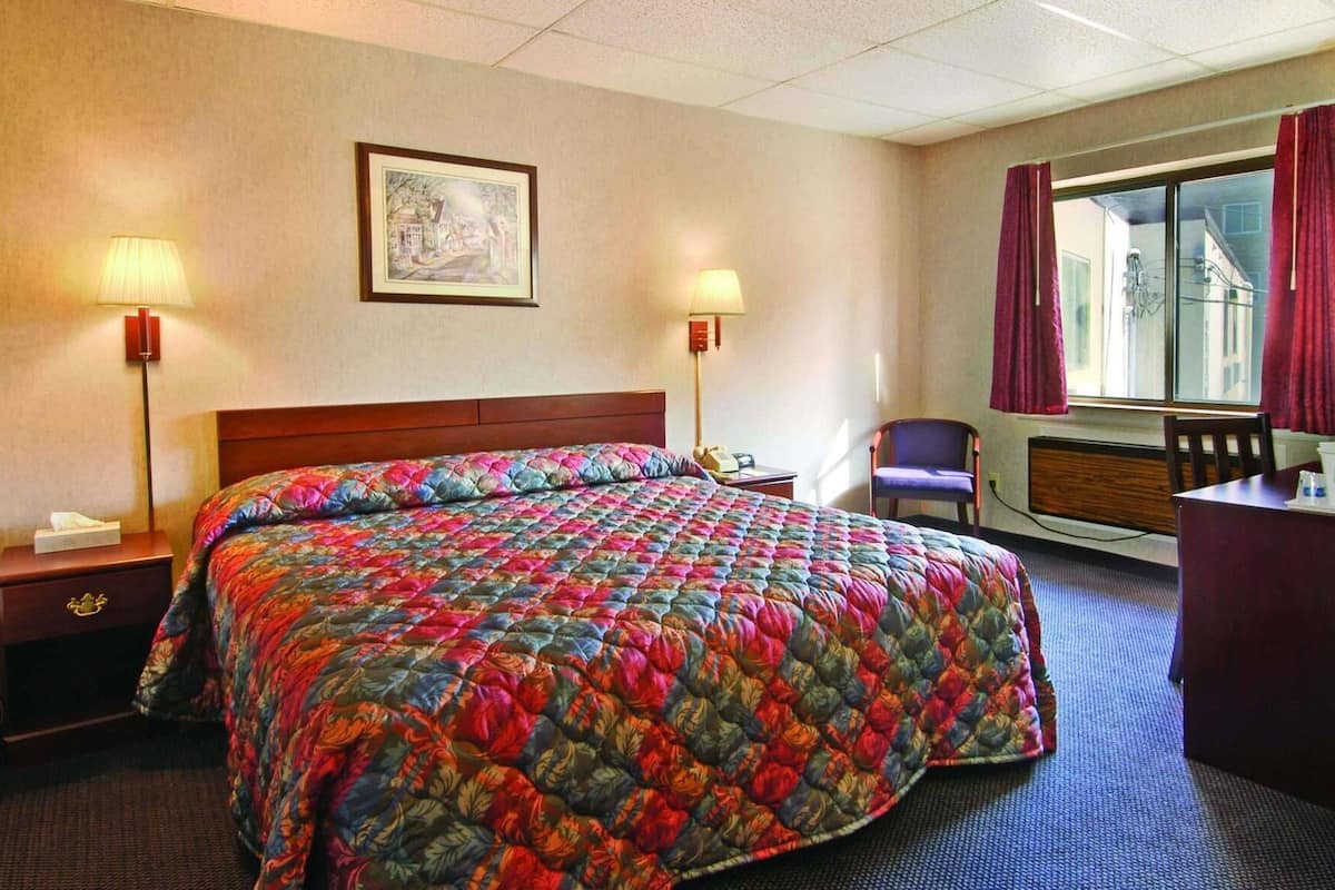 A hotel room with a large bed, two bedside lamps, a chair, a desk, and a window with curtains.