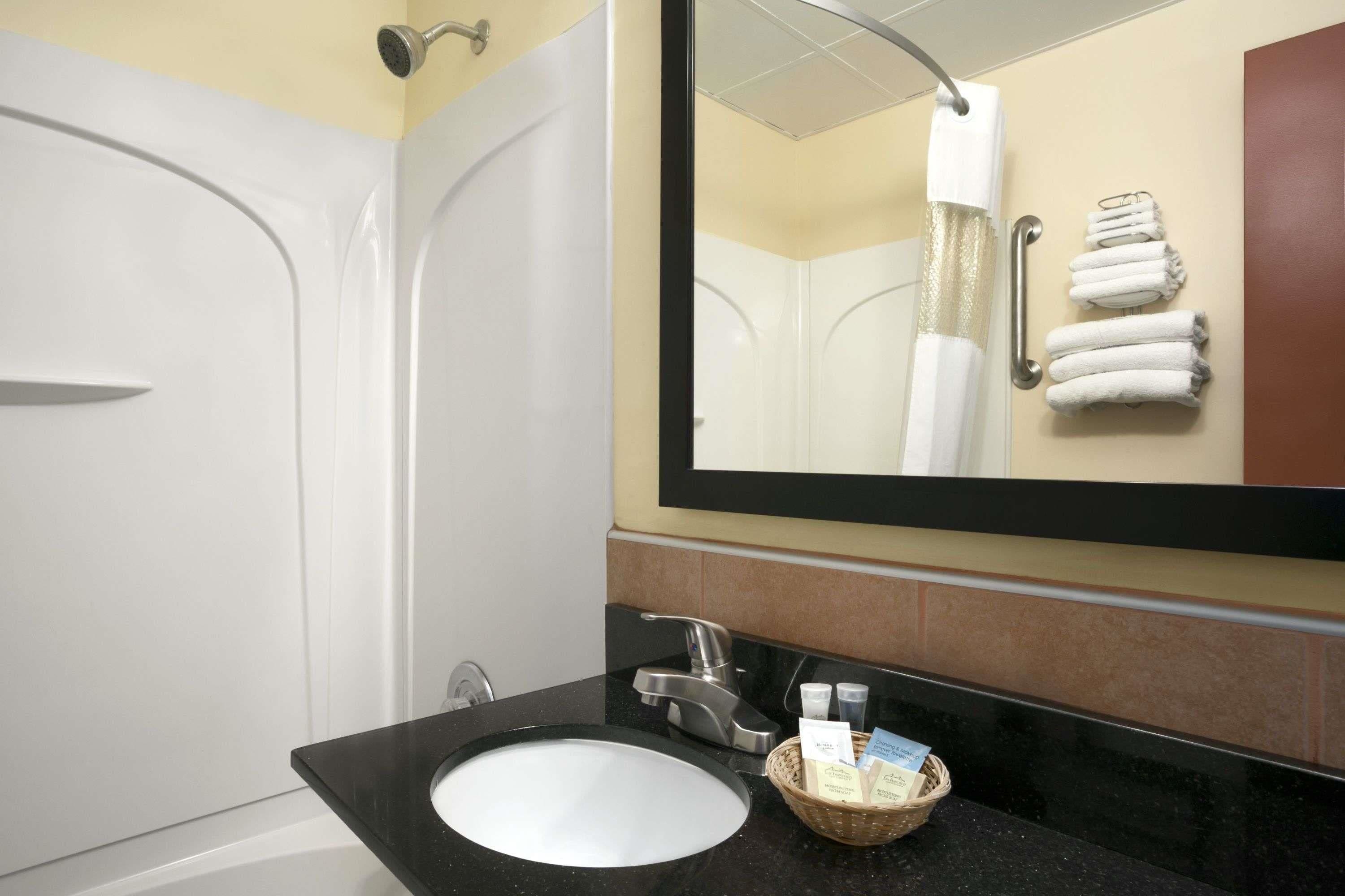 A bathroom with a bathtub, a sink with a black countertop, a mirror, and a towel rack with towels.