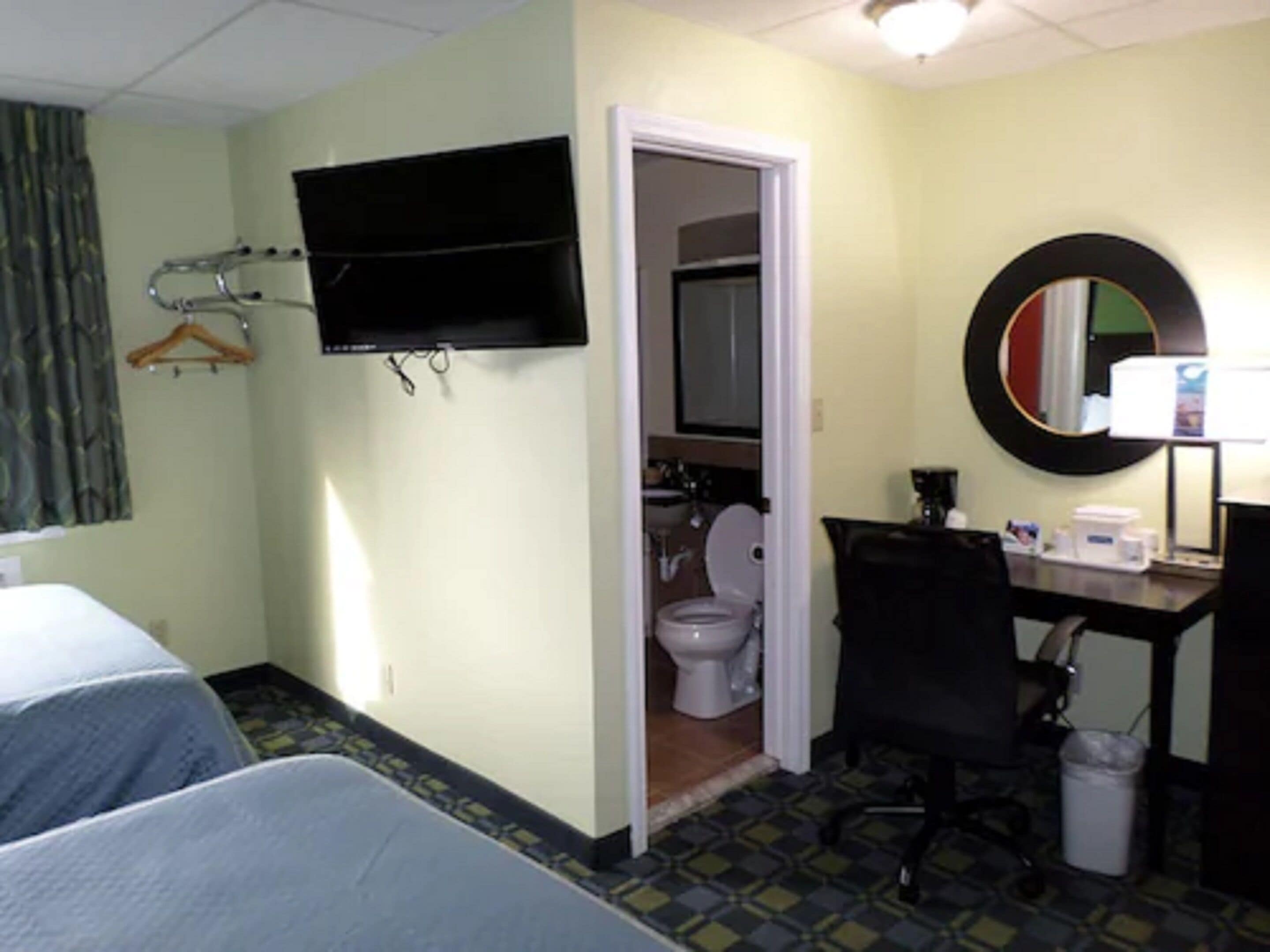 Quarto de hotel com cama, escrivaninha, cadeira, televisão e banheiro.
