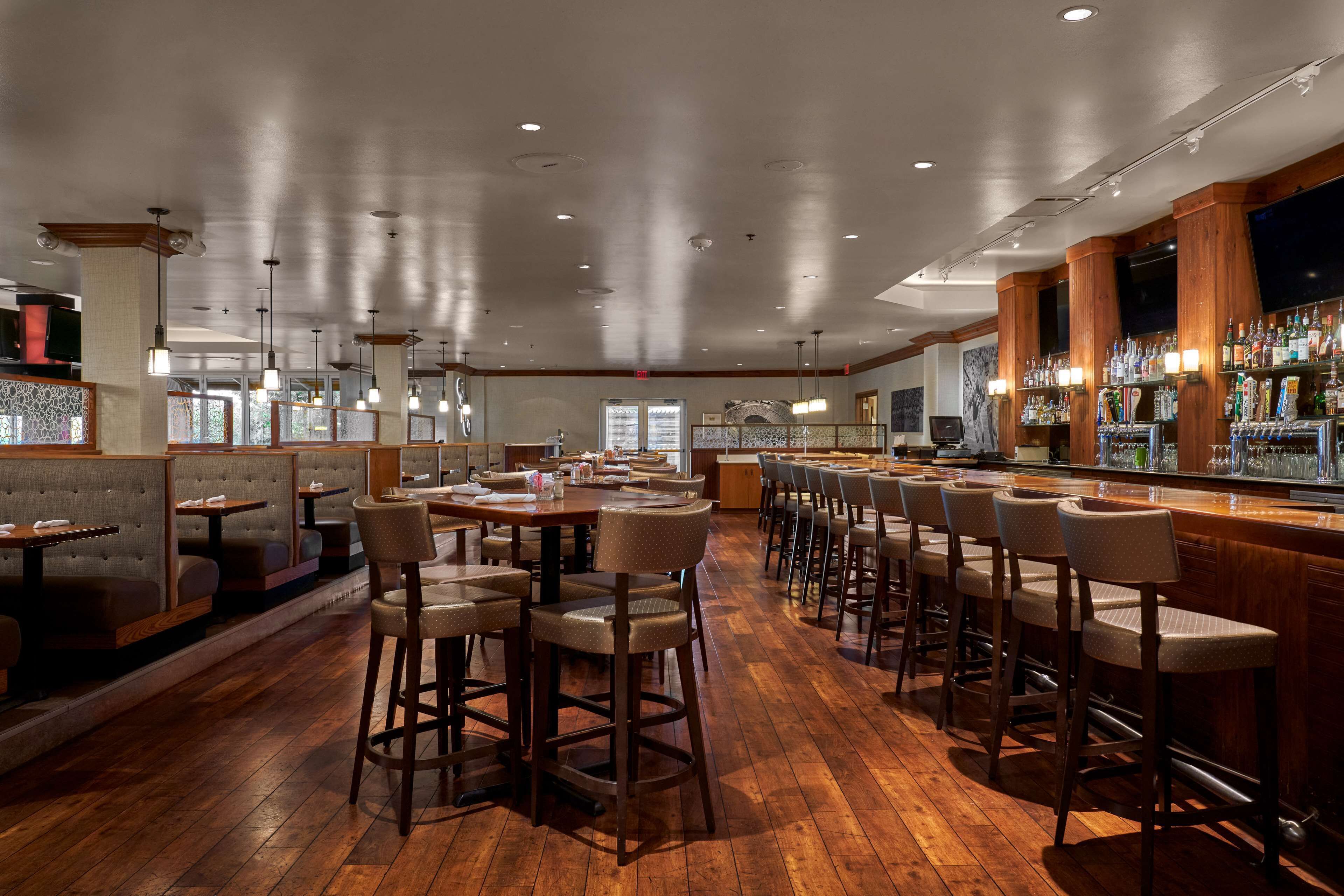 Een restaurant met houten vloer, barstoelen en tafels.