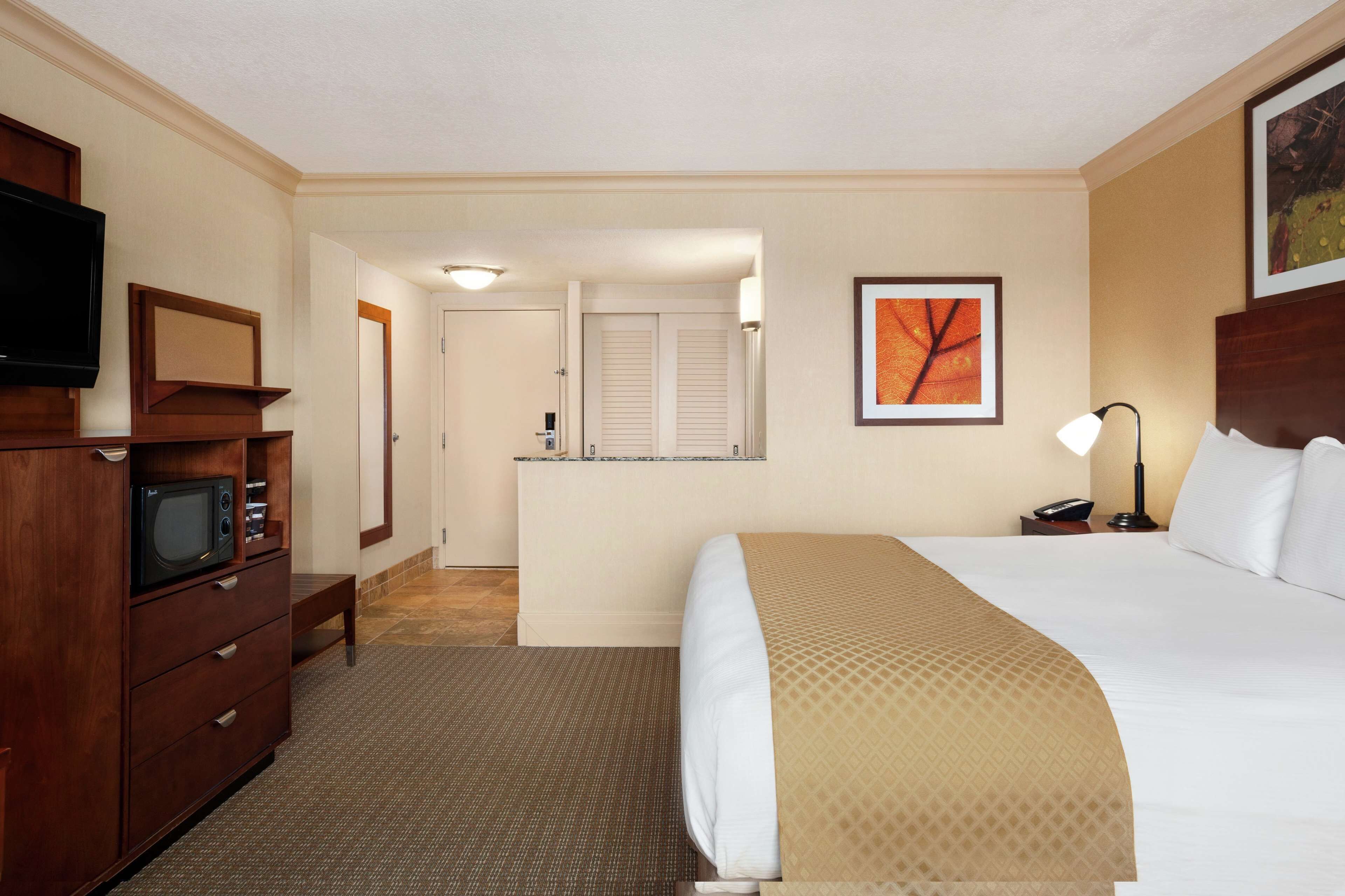 A hotel room with a bed, a TV, a desk, and a bathroom visible through an open door.