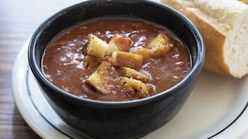 A bowl of soup with croutons and a slice of bread on a plate.
