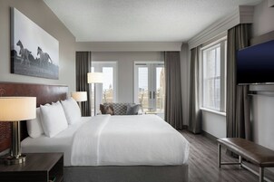 Una habitación de hotel con una cama grande, un banco, un televisor y vistas a la ciudad.