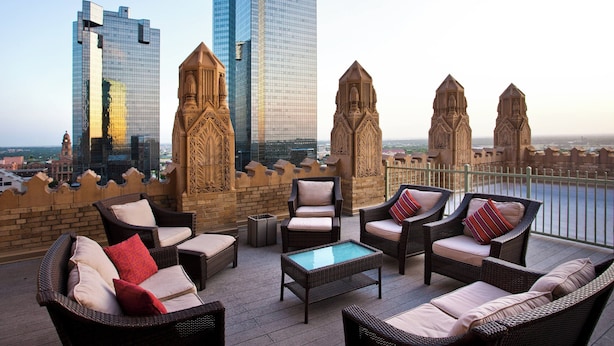Une terrasse sur le toit, aménagée avec des meubles en osier, une table en verre, et offrant une vue sur les gratte-ciel modernes et les bâtiments historiques.