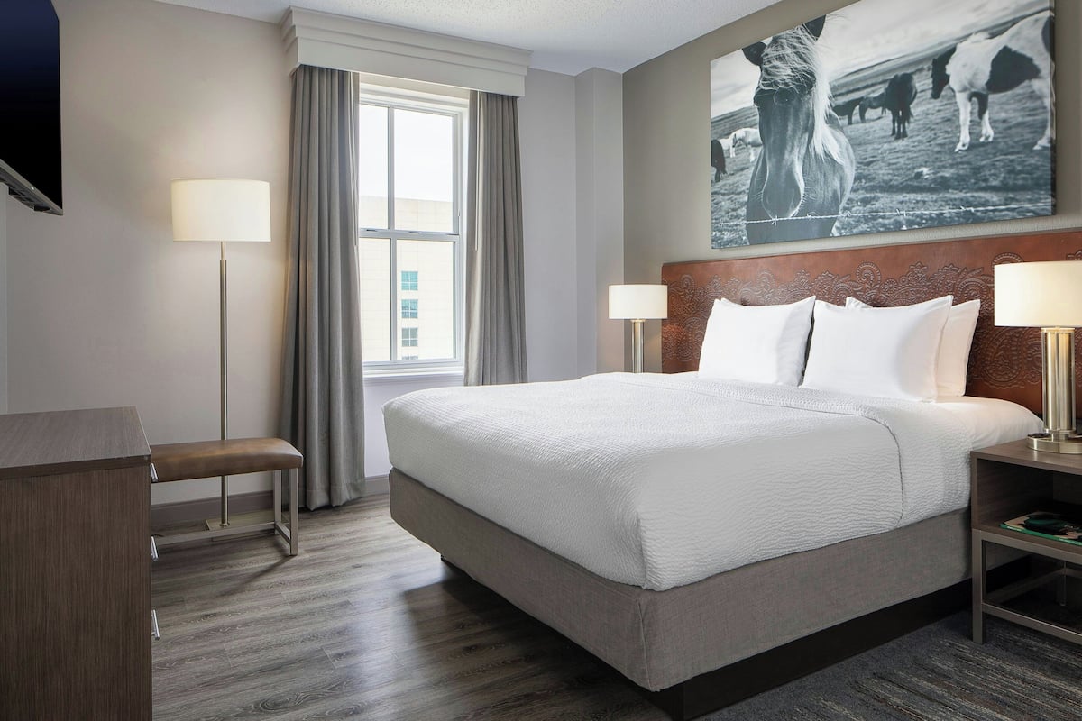 Een hotelkamer met een groot bed, een bankje, een bureau, een televisie en een schilderij aan de muur.