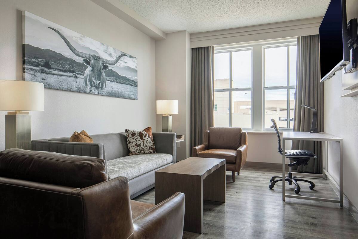 Een moderne hotelkamer met een bank, fauteuils, een bureau en een groot raam.