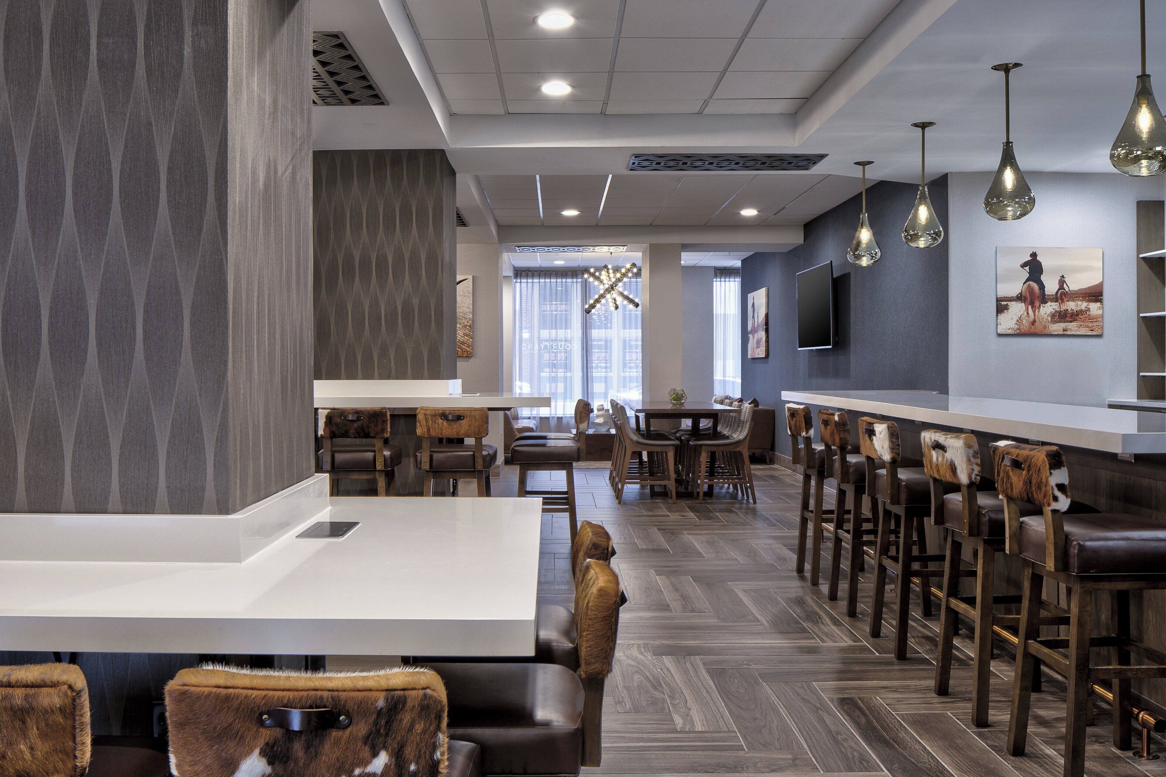 A modern restaurant with a long counter, wooden chairs, and hanging pendant lights.