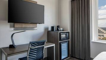 Une chambre d’hôtel équipée d’un téléviseur à écran plat fixé au mur, d’un bureau avec une chaise, d’un four à micro-ondes et d’un mini-réfrigérateur.