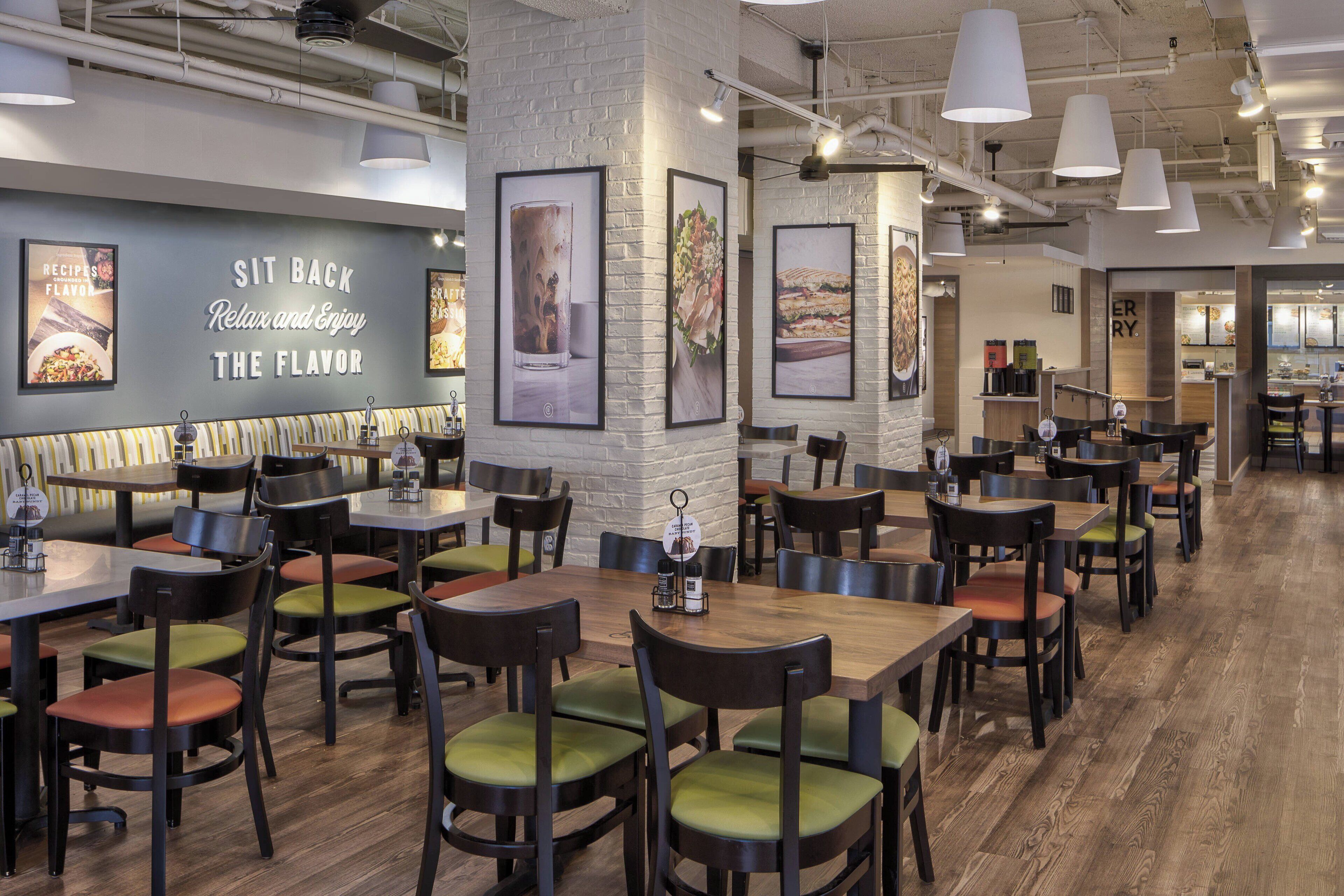 A restaurant interior with wooden tables and chairs, framed artwork on the walls, and a sign that reads "SIT BACK Relax and Enjoy THE FLAVOR".