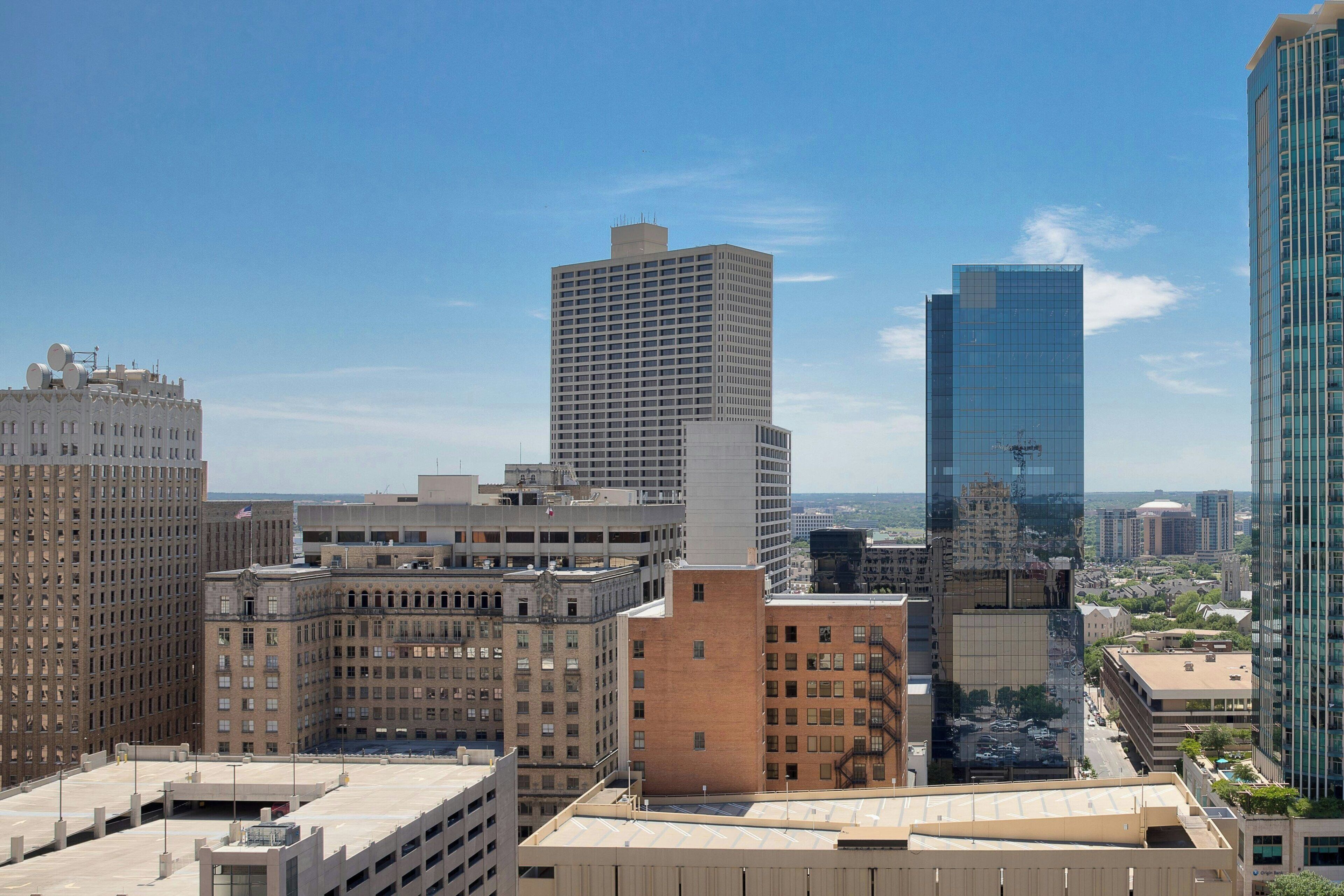 A cityscape with various high-rise buildings, including a prominent glass skyscraper and a mix of older, brick structures.
