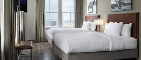 A hotel room with a large bed, a TV mounted on the wall, and a window with a city view.