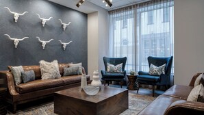 Un salon moderne avec un canapé en cuir marron, deux fauteuils bleus, une table basse et un mur orné de crânes de vache.