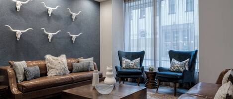 A modern living room with a brown leather sofa, two blue armchairs, a coffee table, and a wall with mounted cow skulls.