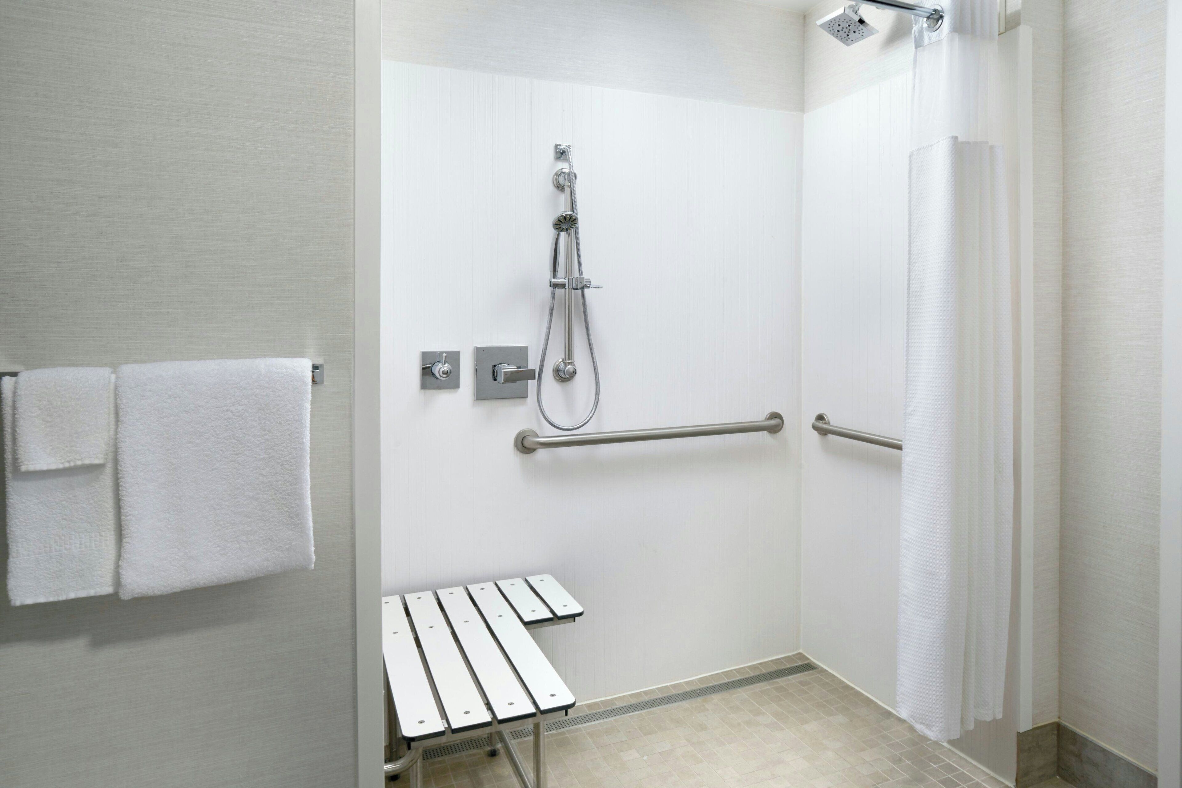 A bathroom with a shower, a bench, and a towel rack.