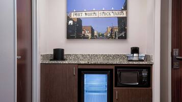 Una kitchenette con microondas, cafetera y refrigerador. Sobre la kitchenette, una foto enmarcada de una señal de calle.