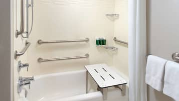 Baño con bañera blanca, barras de apoyo, cabezal de ducha y toallero.