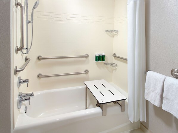 Baño con bañera blanca, barras de apoyo, cabezal de ducha y toallero.