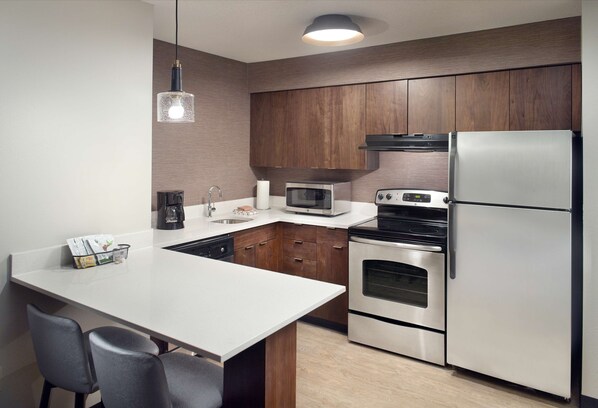 Una cocina moderna con armarios de madera, un refrigerador de acero inoxidable, un microondas, un horno y un comedor con sillas.