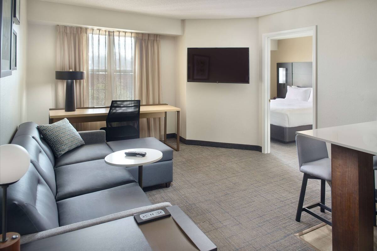 A hotel room with a sofa, a desk, a flat-screen TV, a bed, and a small table.