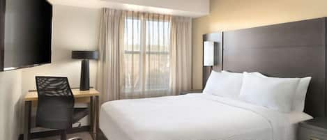 Habitación de hotel con cama, escritorio, silla, televisor y ventana con cortinas.