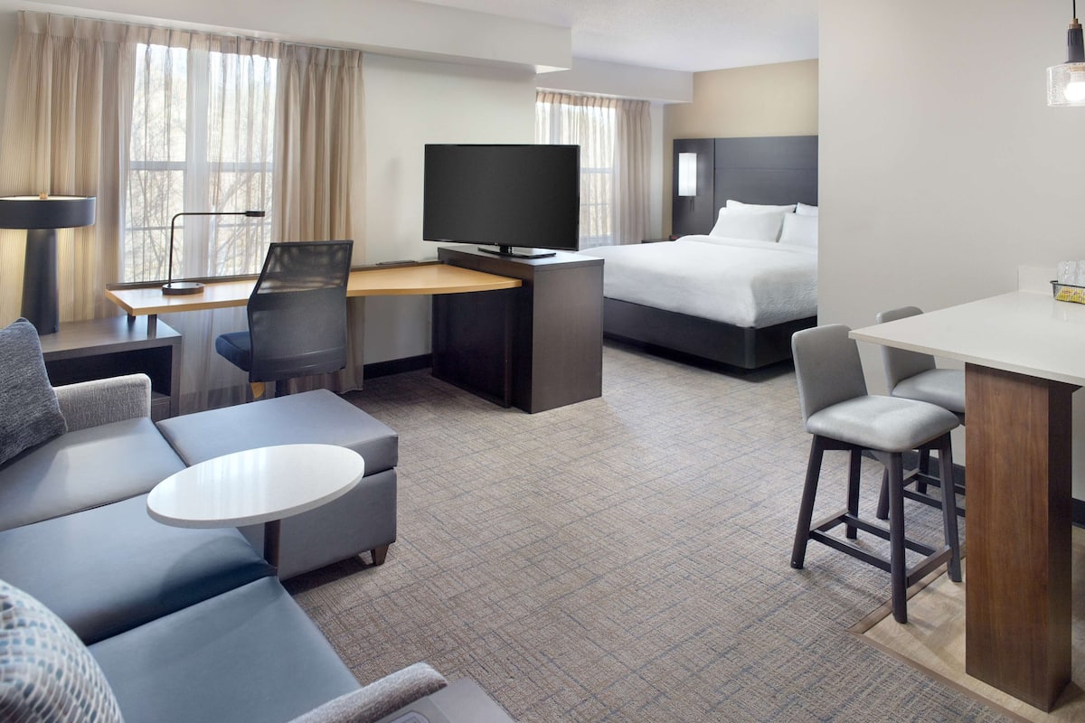 A hotel room with a bed, a desk with a TV, a sofa, and a small dining area.