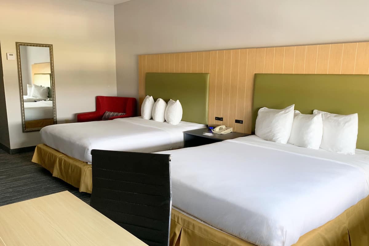 Una habitación de hotel con dos camas, una silla roja, un escritorio con teléfono y un espejo.