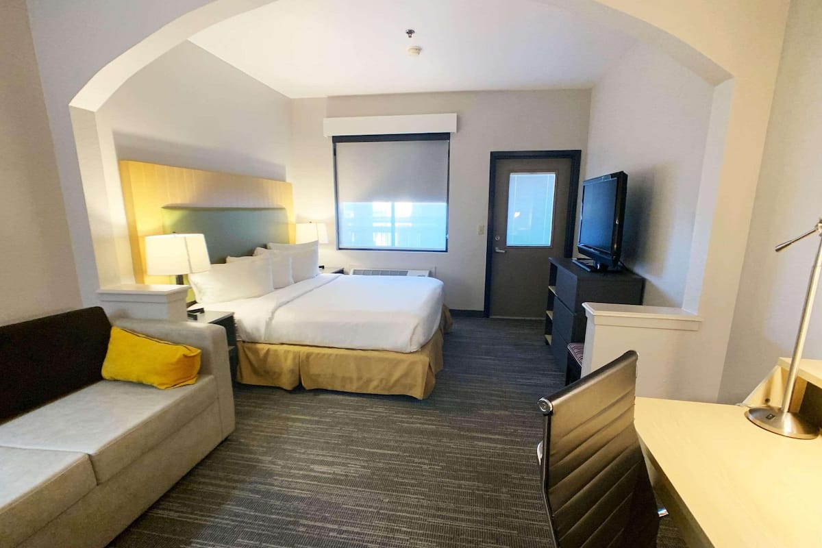 Una habitación de hotel con cama, sofá, escritorio, televisor y ventana.