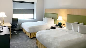 Une chambre d’hôtel avec deux lits, un bureau, une chaise, une lampe et une fenêtre avec des stores.