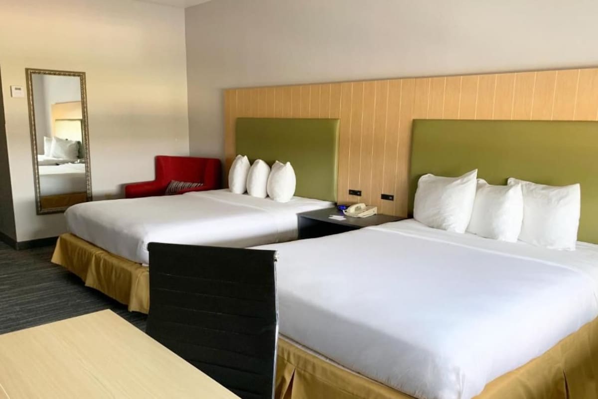 A hotel room with two beds, a red chair, a bedside table, and a mirror.