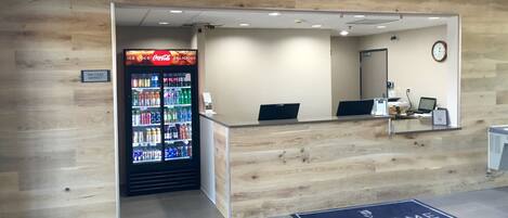 A reception area with a Coca-Cola refrigerator, a welcome mat, and a clock on the wall.