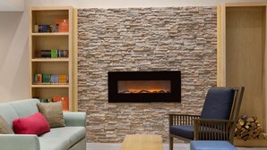 A living room with a stone wall, a fireplace, a bookshelf, a sofa, a chair, and a coffee table. - Country Inn & Suites by Radisson, Fort Worth West l-30 NAS JRB (Fort Worth)