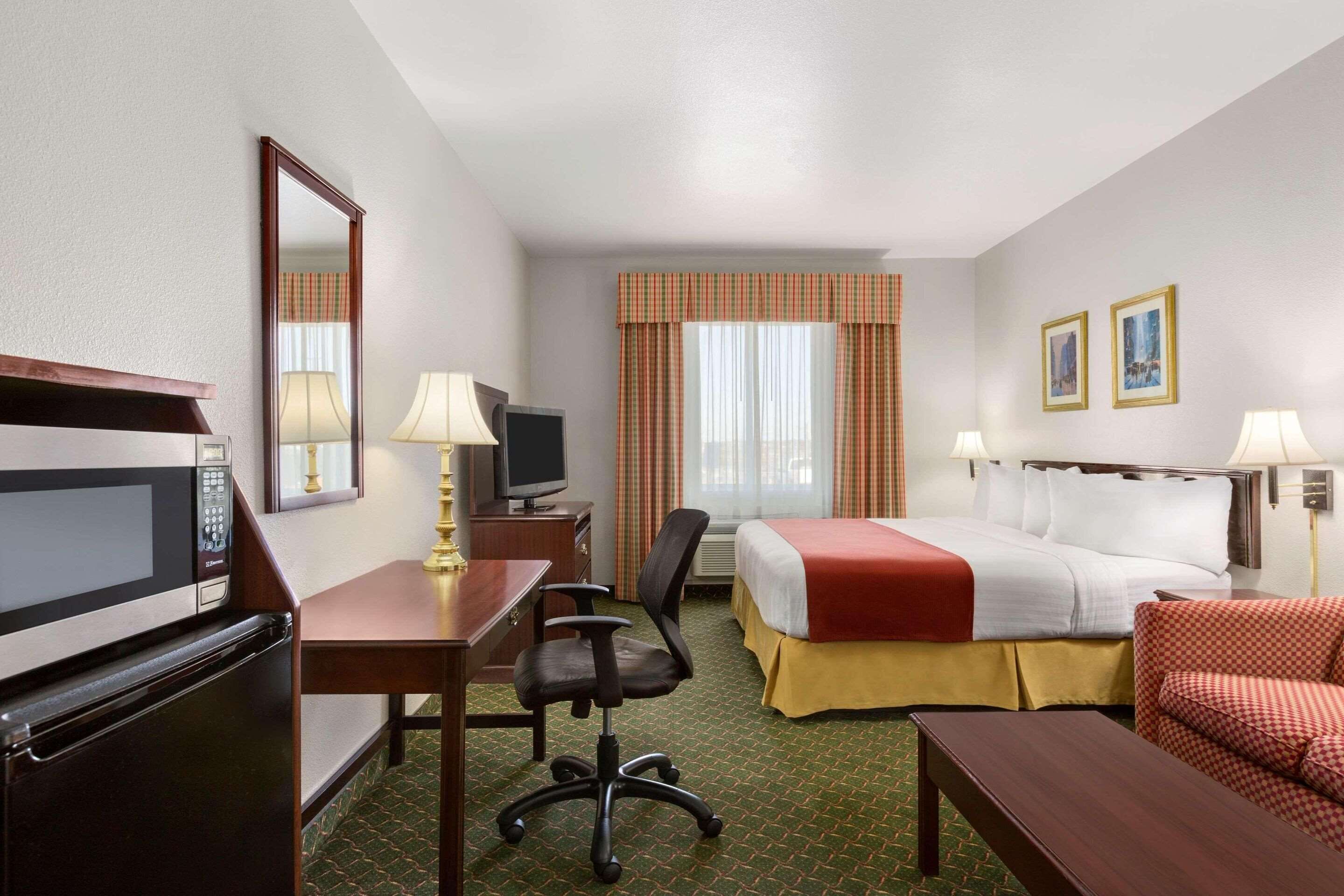 A hotel room with a bed, desk, chair, television, and a microwave.