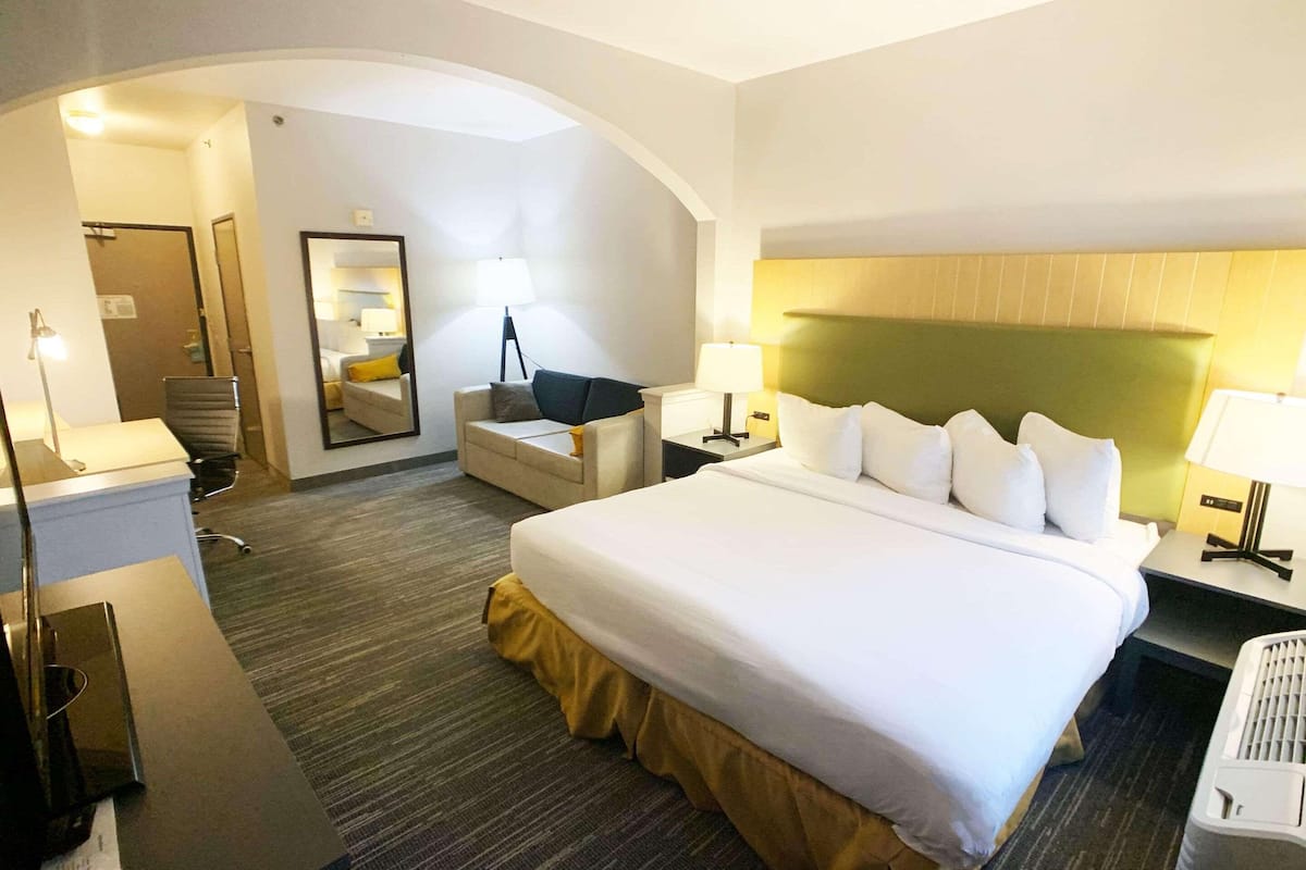 Una habitación de hotel con una cama grande, un escritorio, una silla y una lámpara de escritorio.