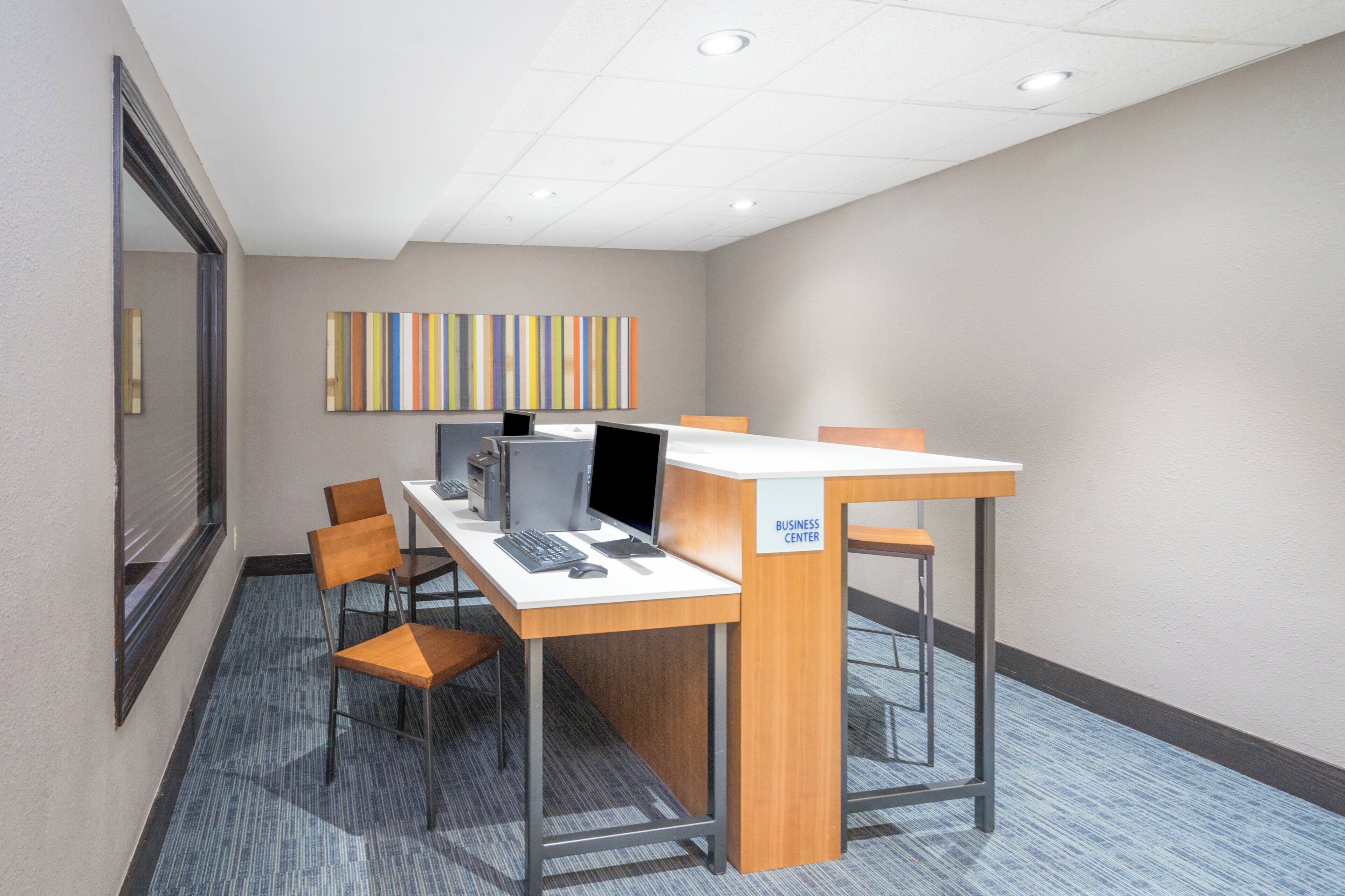 A business center with a desk, computer, and chairs.