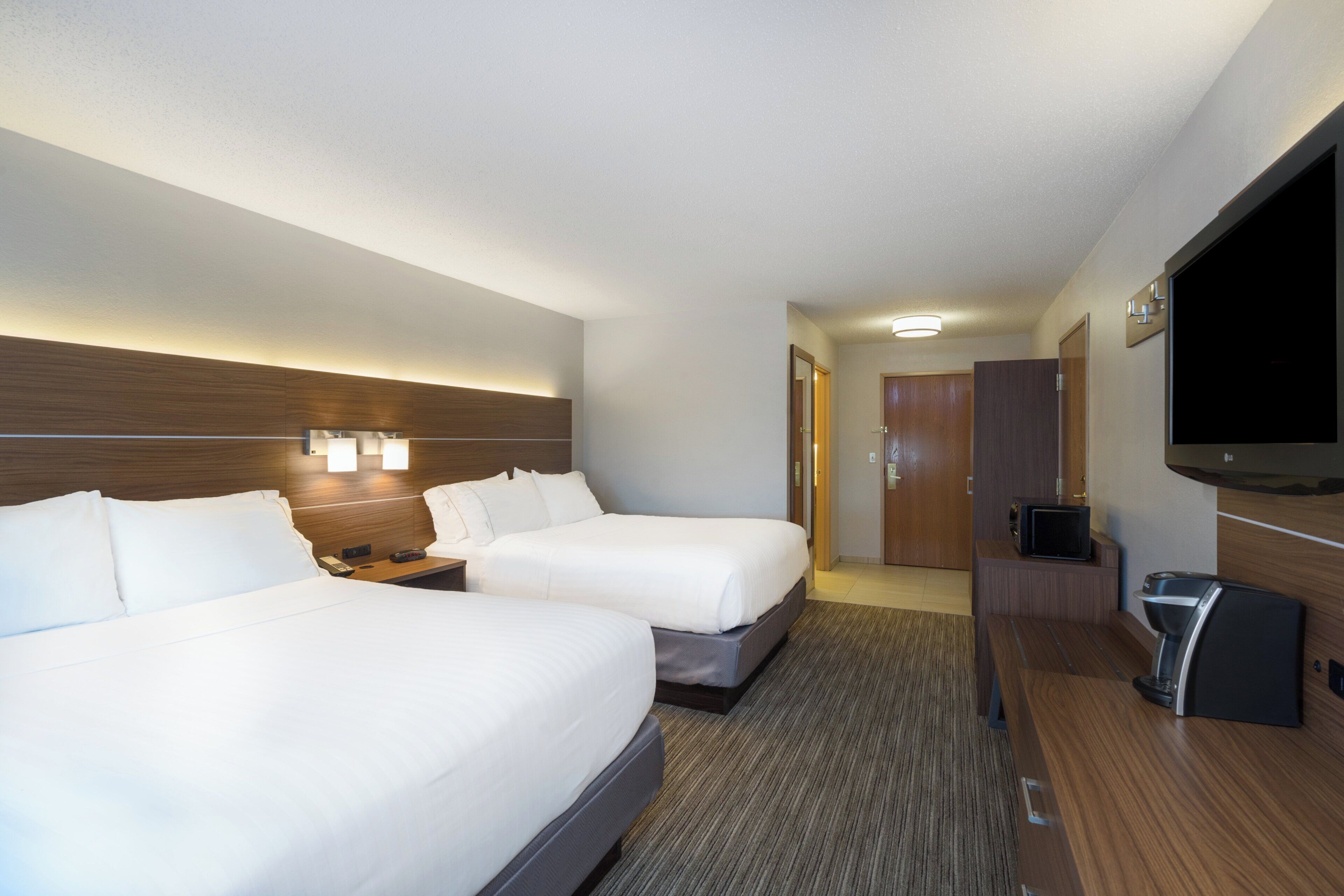 Quarto de hotel com duas camas, televisão, minibar e porta de acesso a um banheiro.