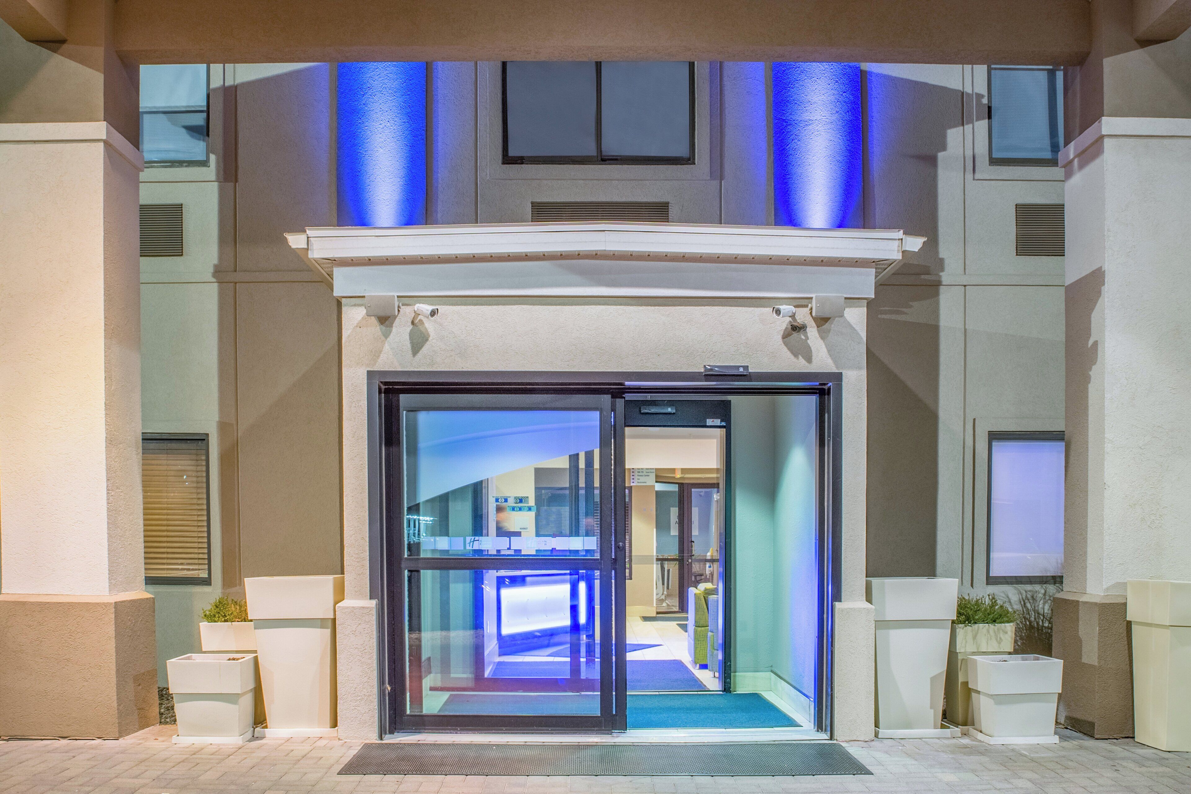 Entrada de hotel com porta de vidro, teto iluminado em azul e corredor interno visível.