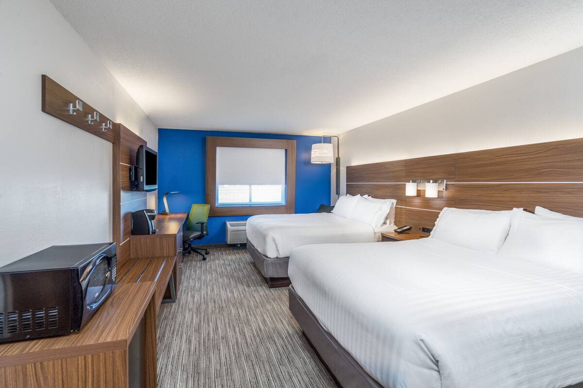 A hotel room with two beds, a desk with a microwave, a TV, and a window with blinds.