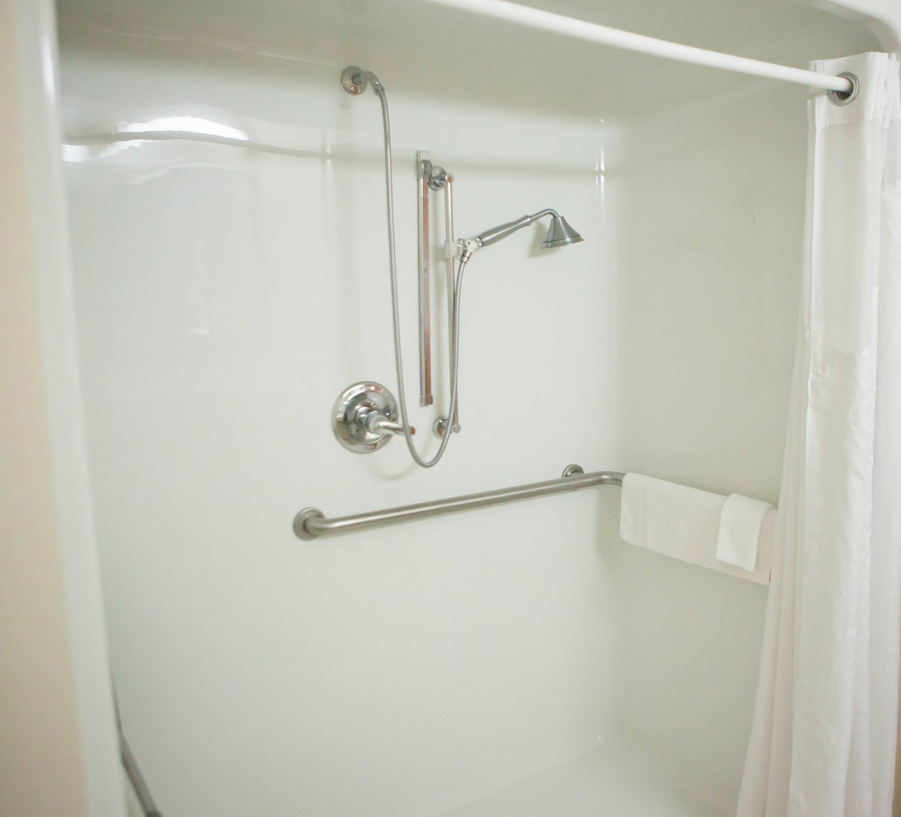 Ducha con cabezal de ducha de mano, grifo empotrado en la pared y barra de apoyo.