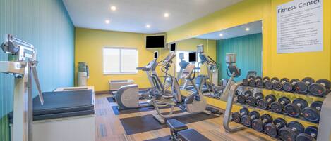Un gimnasio con equipamiento de ejercicio, mancuernas y una cinta de correr.
