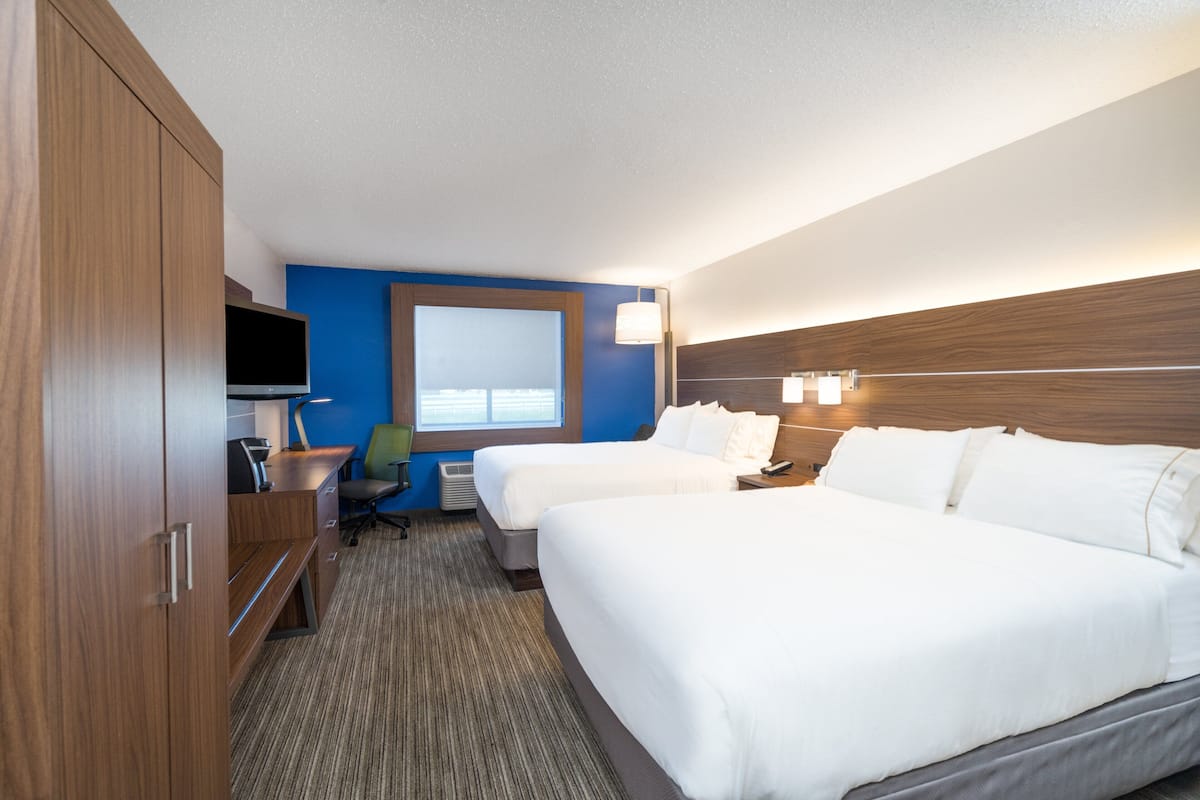 A hotel room with two beds, a desk with a chair, a TV, and a window with blinds.